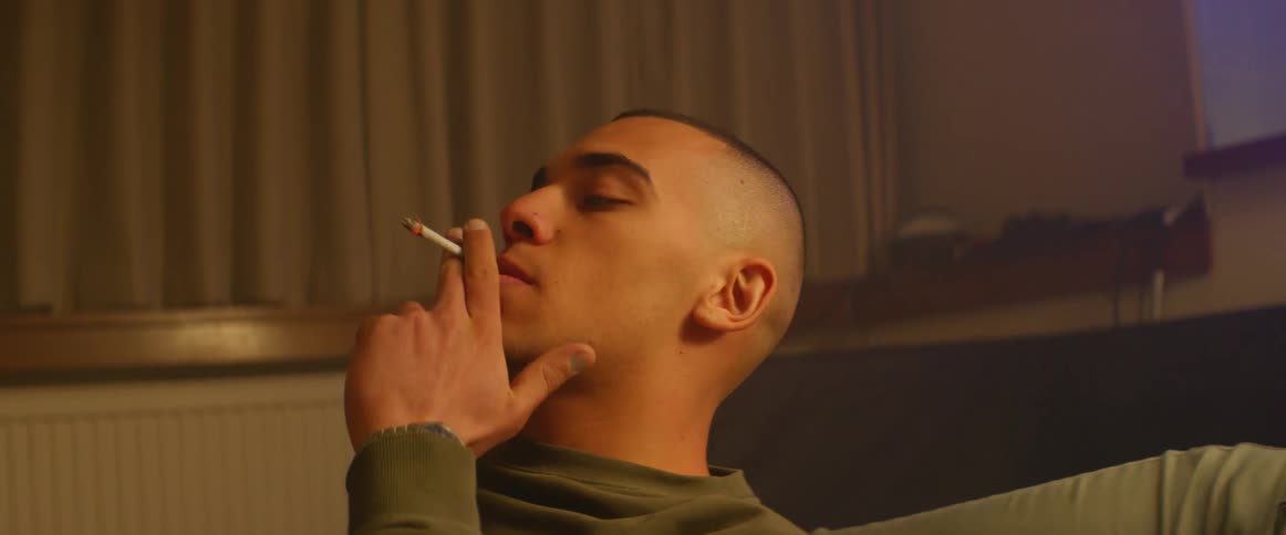 A girl hands a young man a cigarette and he smokes it