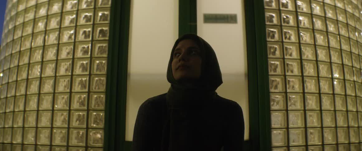 A woman stands outside a building with tall glass walls at night