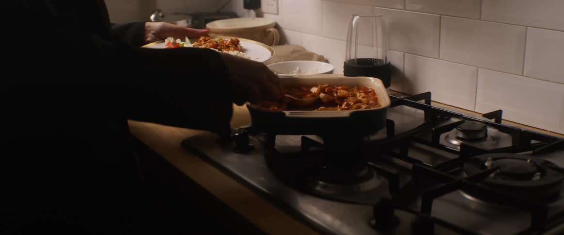 A woman puts food from a casserole dish onto her plate in her kitchen