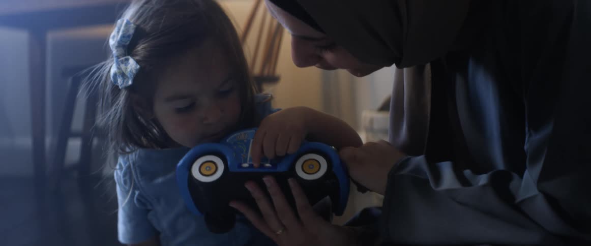 Mother wearing a hijab and daughter playing with a toy car in a house