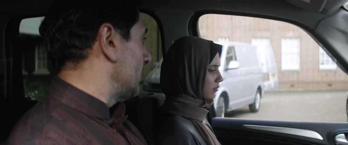 A man looks over to the woman sitting in the car with him