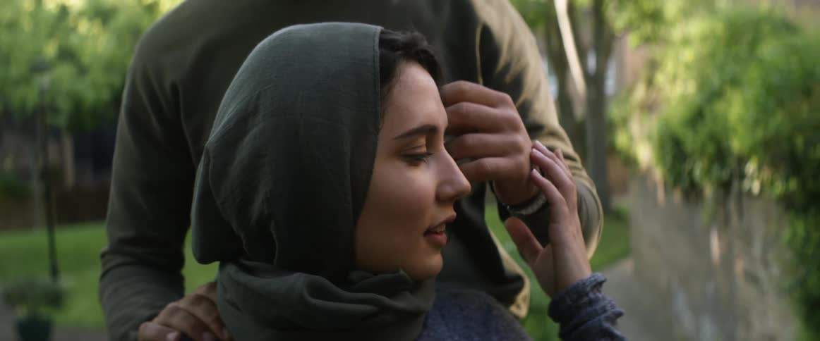 Man tenderly touches hair of a woman wearing a hijab in the backyard
