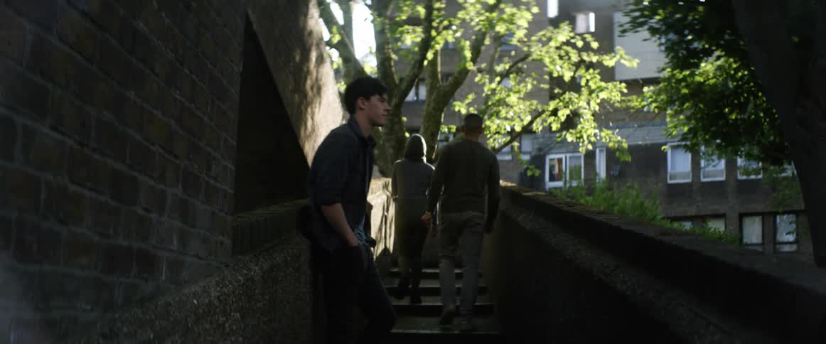 Two men and a woman on a staircase then walking upstairs with trees and buildings in the background