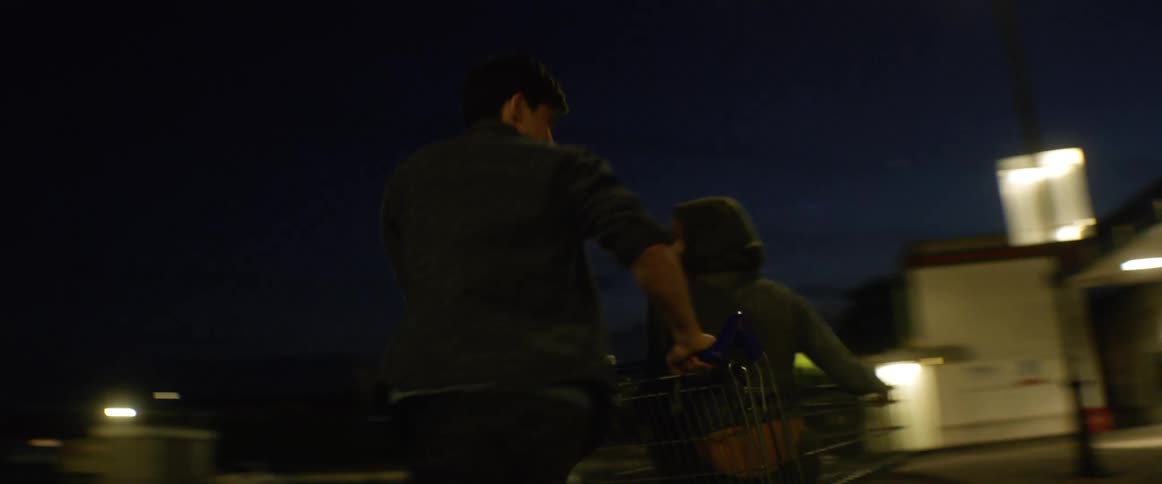 A male teenager twirls a female around in a shopping car in a store parking lot