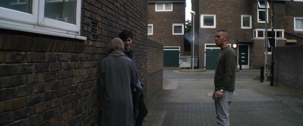 Woman riding skateboard joins two men kissing one and borrowing cigarette from the other