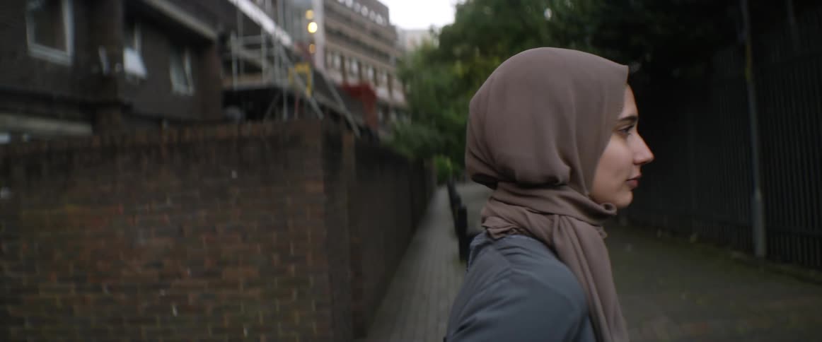 Woman wearing a head covering steps forward and tilts her head back