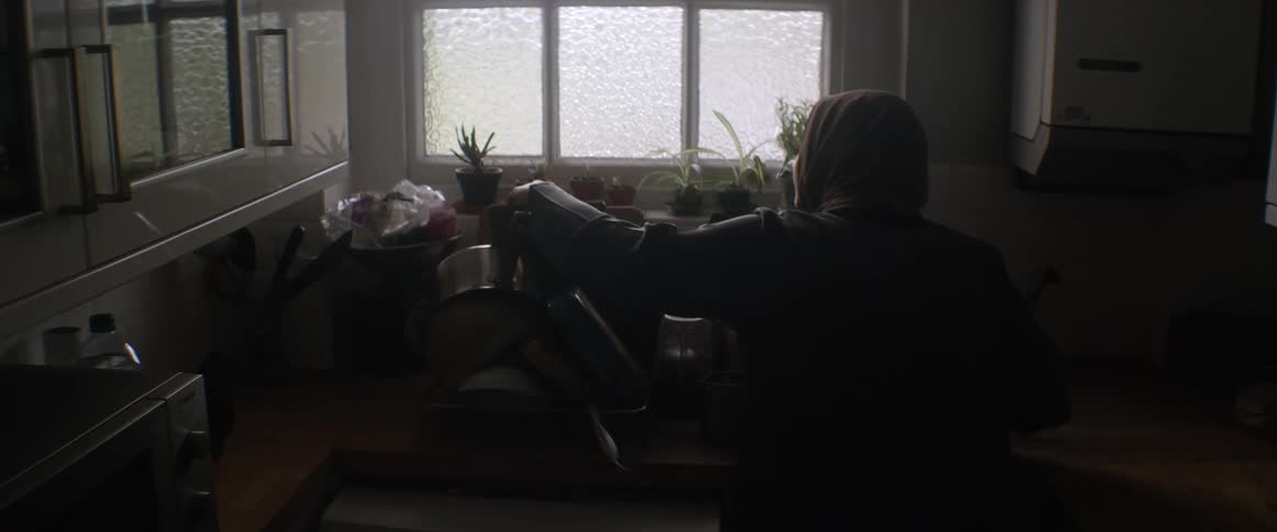 A woman washes dishes in front of a kitchen window