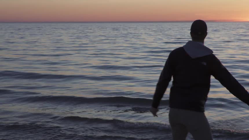 A man throws rocks into the ocean at dusk