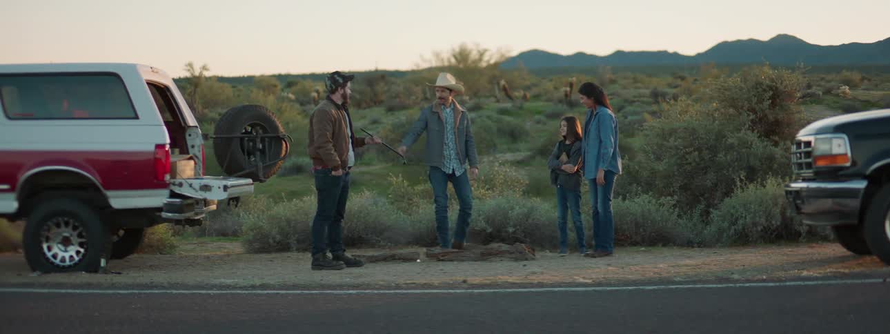 A teenager takes a man a tool and he heads to change his tire with another man