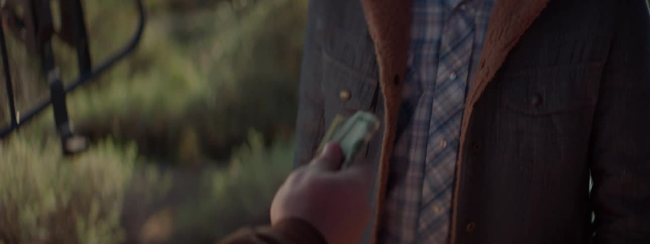 Someone offers dollar bills to a cowboy drinking water from a jug in the desert