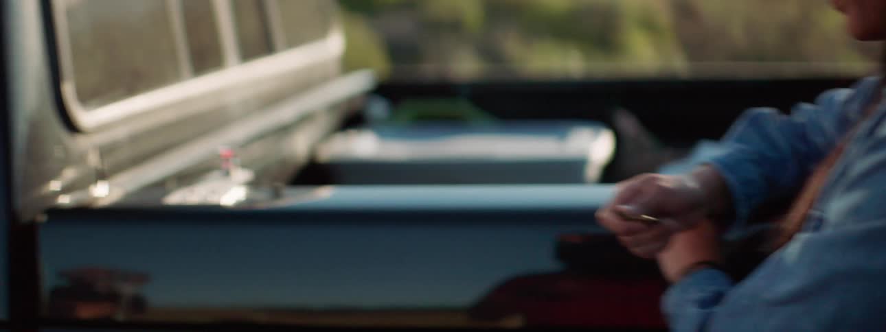 A young girl sits inside a truck and eats while a young woman waits outside the truck