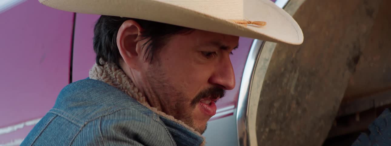 A man in a cowboy hat crouches next to a car