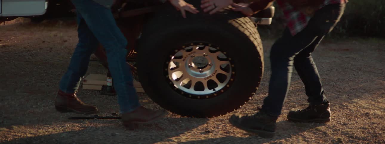 Two men are pushing a wheel into a truck