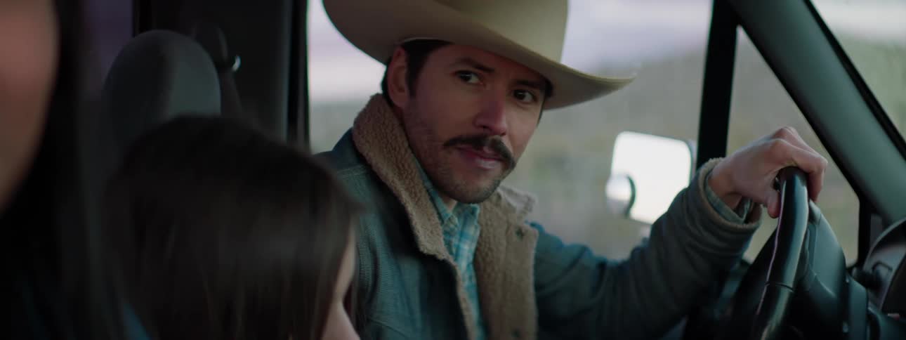A man in a cowboy hat sitting in the drivers seat of a vehicle looks at the girl and woman sitting beside him