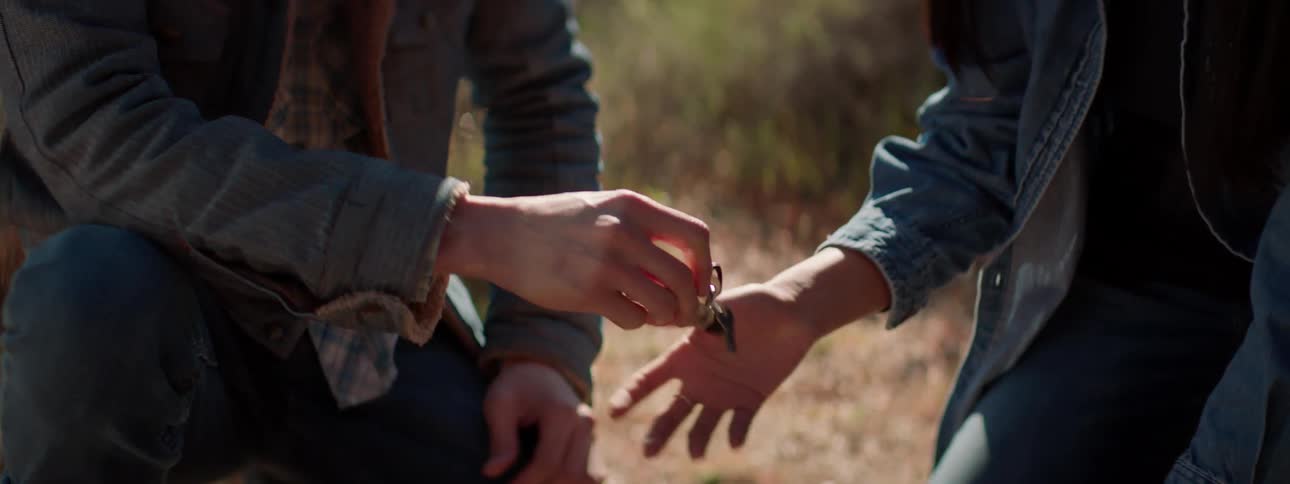Man wearing a cowboy hat hands some keys to a woman as they sit in a field