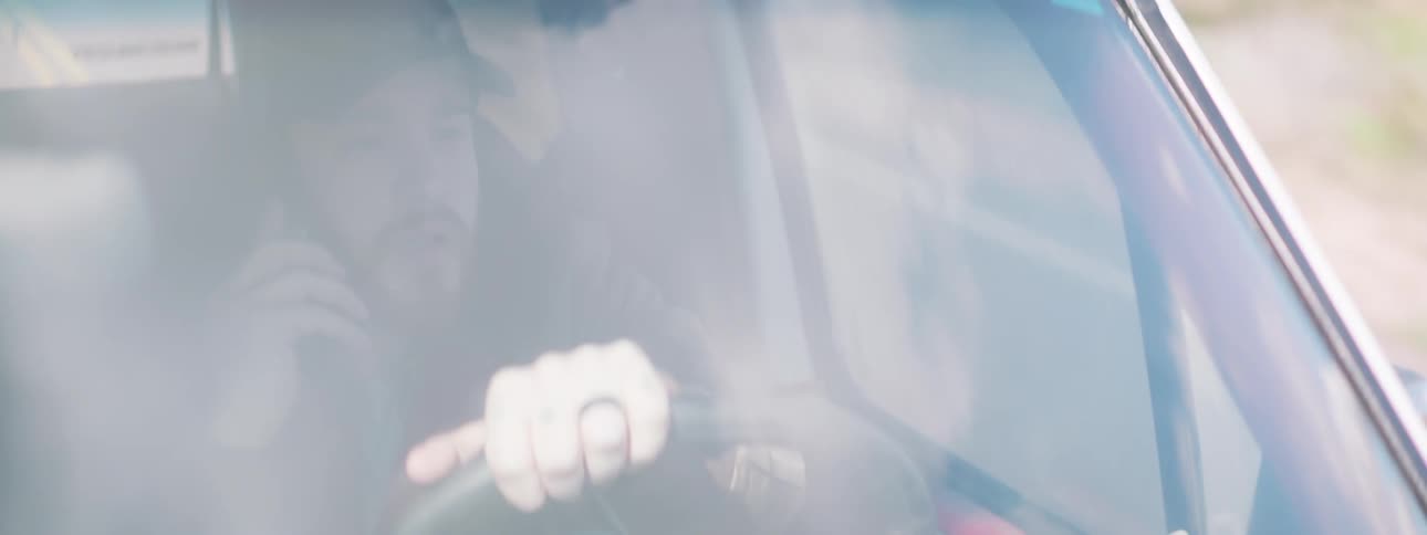 Man with beard and a cap talks on the phone while driving a white four wheel drive
