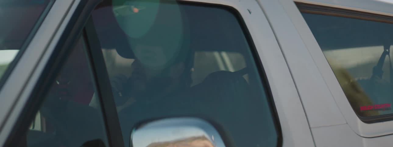 Man with beard and a cap talks on the phone while driving a white four wheel drive