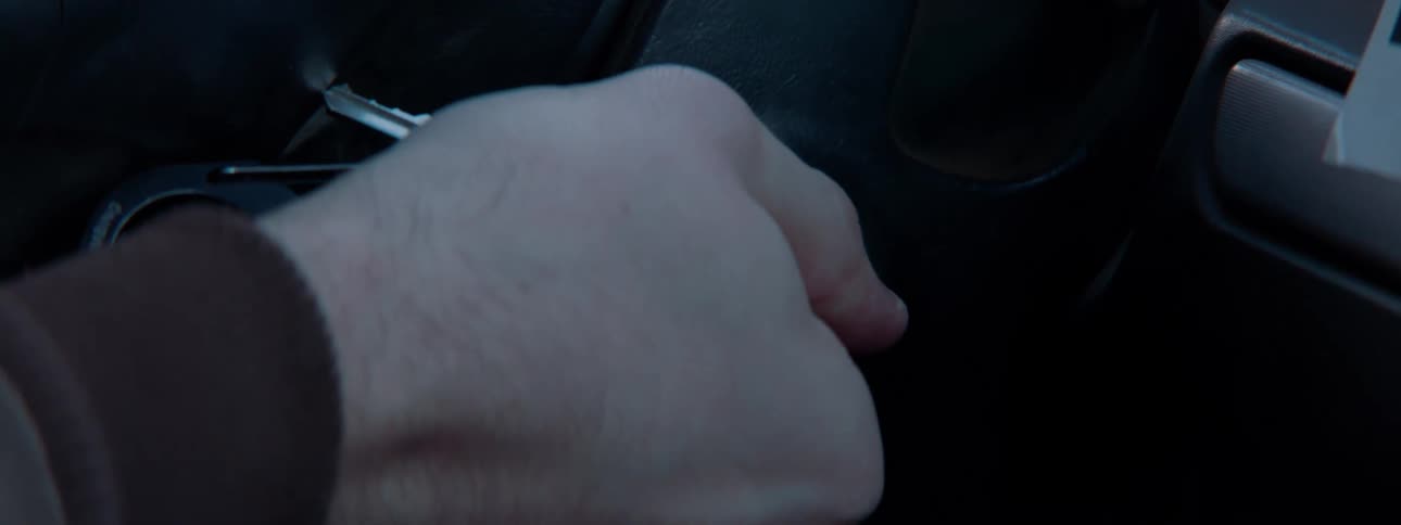 A person inserts a car key into the ignition and twists it to start the vehicle