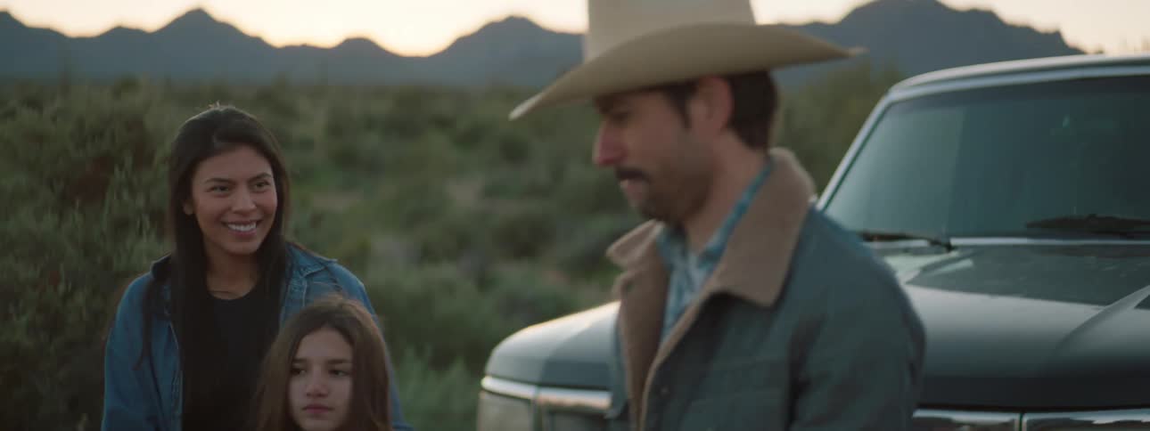 A girl gives a man some food at the side of the road and another man shakes his hands before they get back in their truck