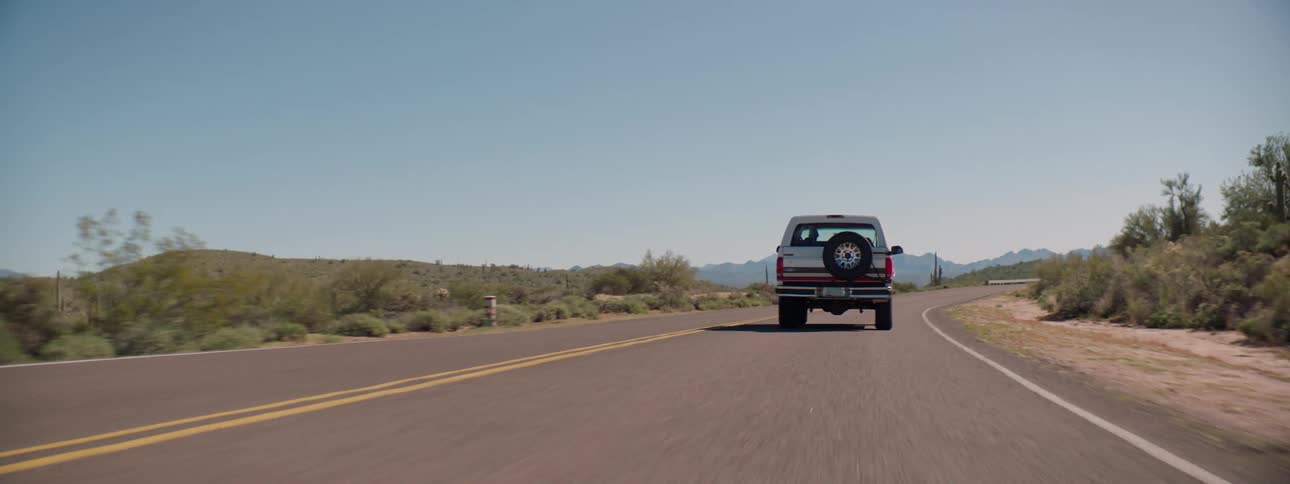 A vehicle driving on a road with hills mountains and the sky in the background