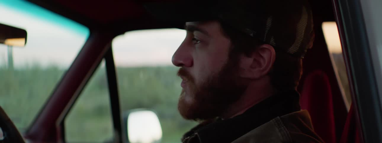 Man with beard and a cap sits in a car and starts cry