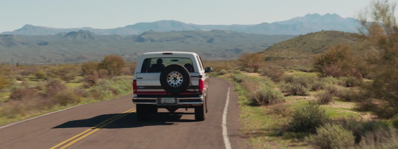 A sport utility vehicle drives down a curvy two lane road near a mountain range