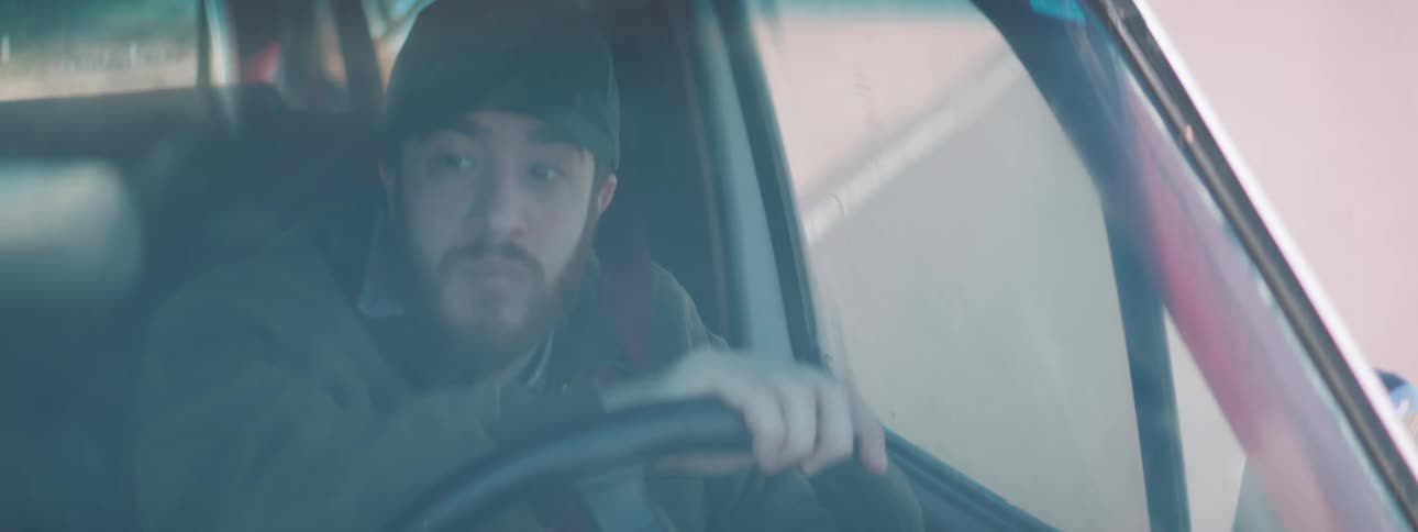 A man with a hat driving a vehicle with the road and plants in the background