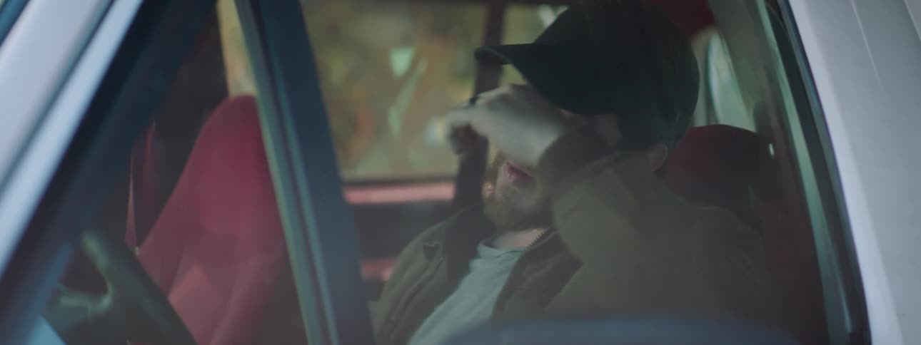 A man talks on his phone while behind the steering wheel of his parked car and hangs up in frustration