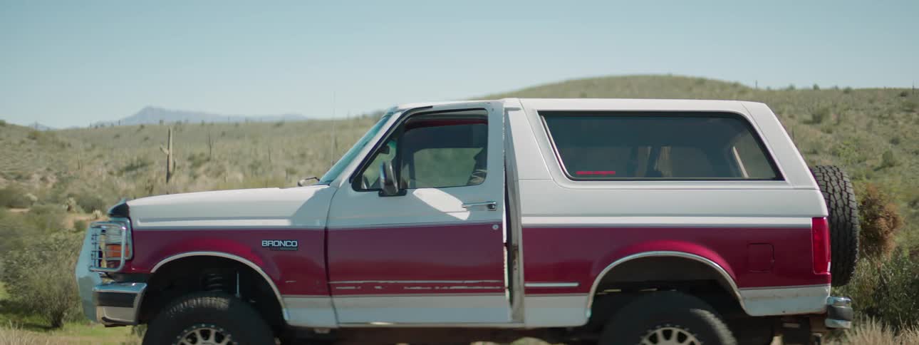 A man closes the trunk of his vehicle thats parked on the side of a road and gets back in to leave