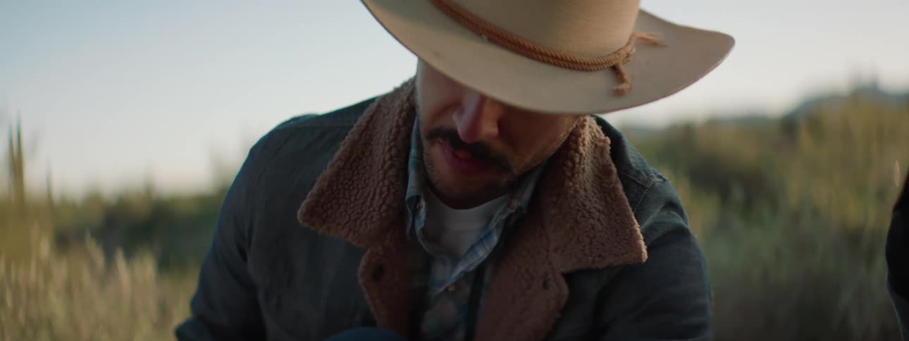Cowboy sits in field talking to woman and others