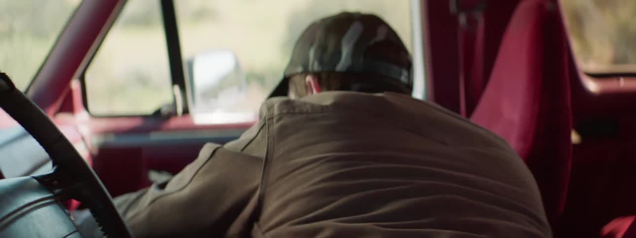 Man with red beard and a cap answers a phone call in a car