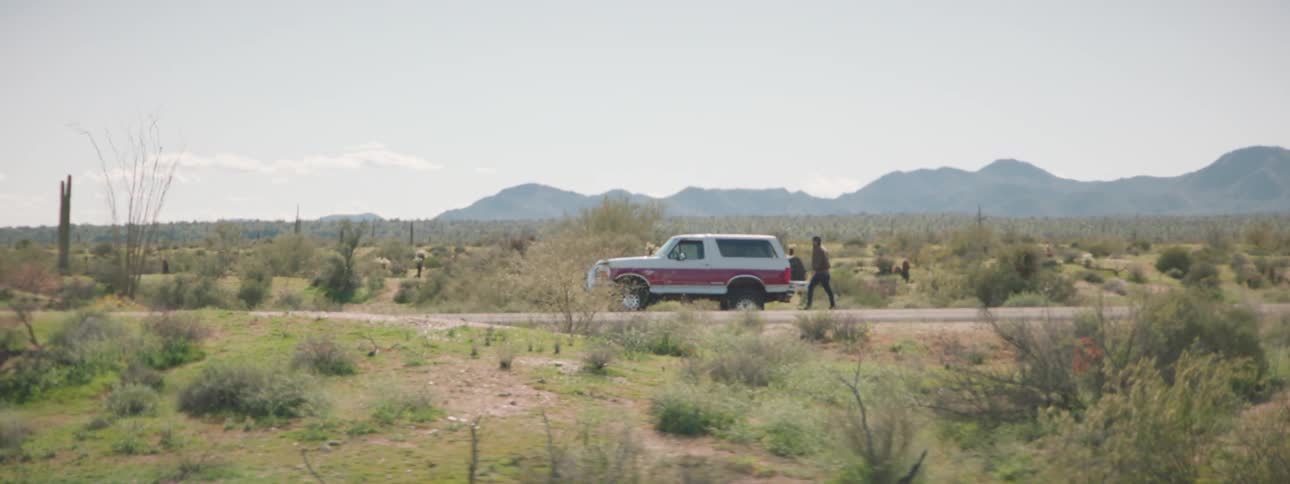 A person sticks his thumb up at a passing vehicle before giving up and entering their own vehicle stopped on the side of the road