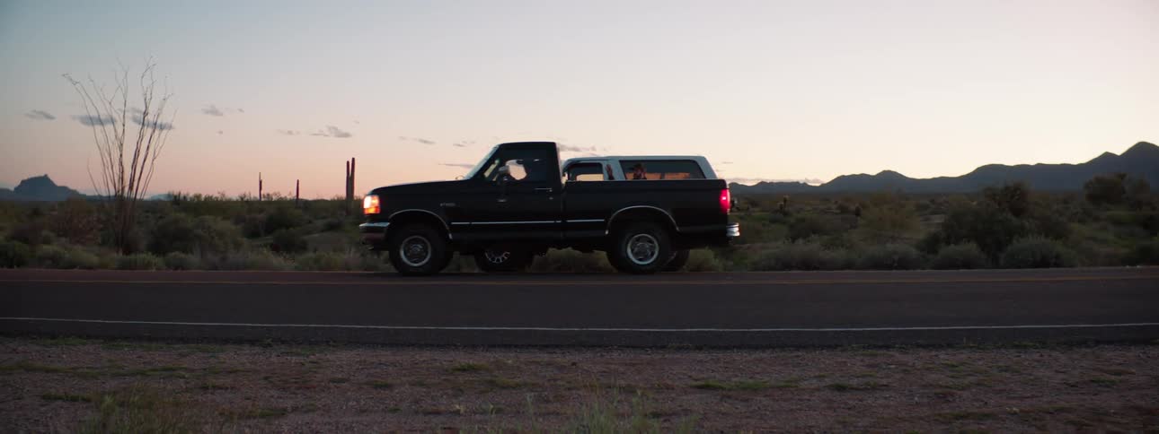 A man standing next to his vehicle on the side of a country road waves as a the truck stopped beside him slowly pulls off
