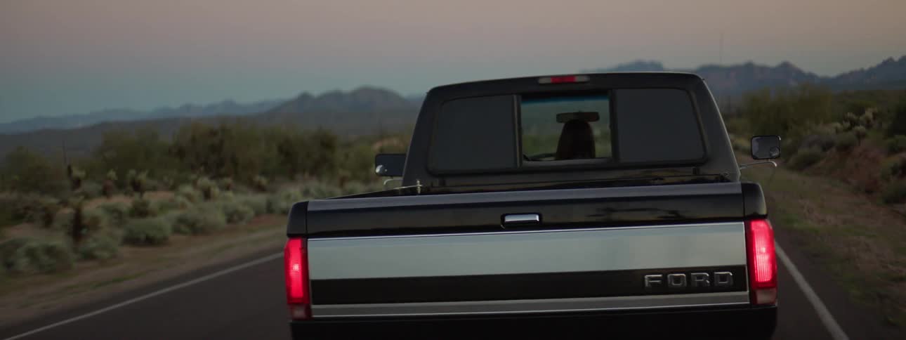 A young girl looks out the back of a truck while it drives down the street