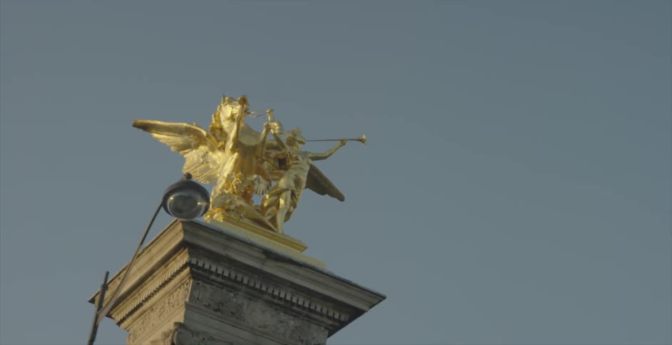 A gold statue sits on a pillar on a cloudy day