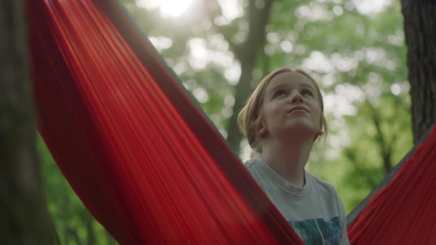A woman sitting on a hammock looking up with trees and the sky in the background