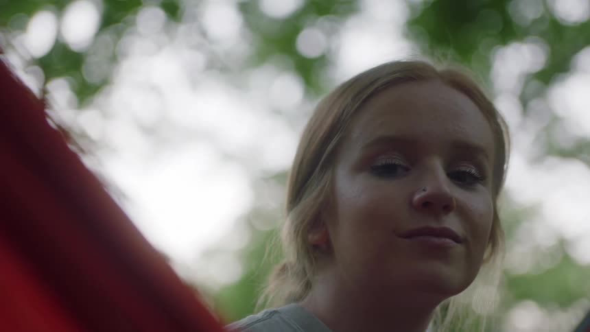 A teenage girl smiles while looking around outside in a hammock