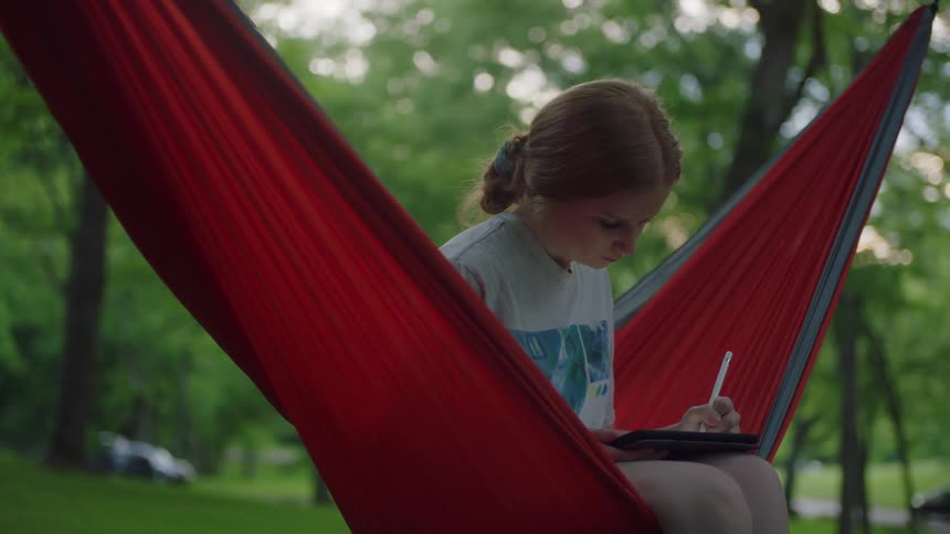 A woman writes on her tablet in a hammock
