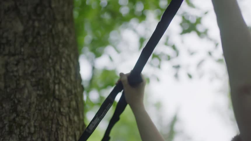 A young girl ties a strap on to a tree