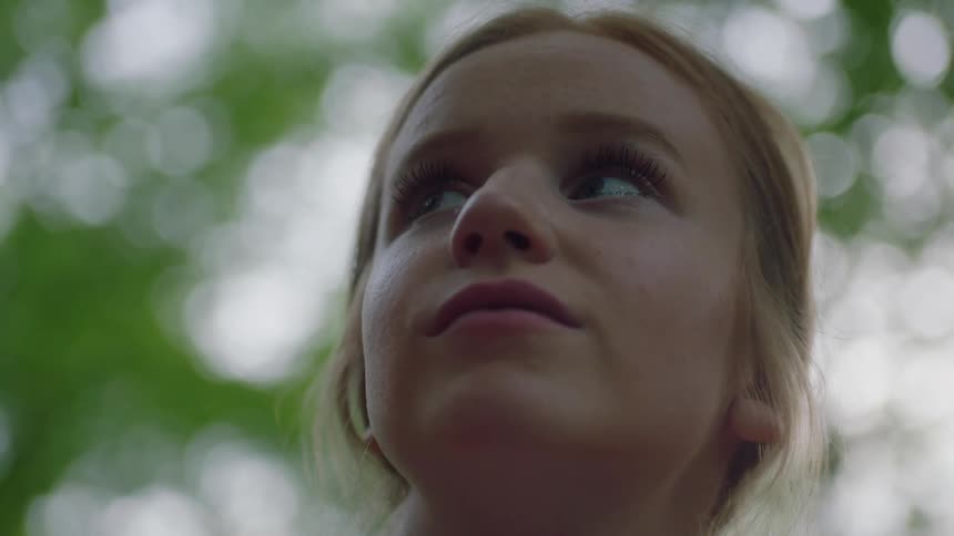 Blonde girl with a pony tail looks around and smiles at the camera in the forest