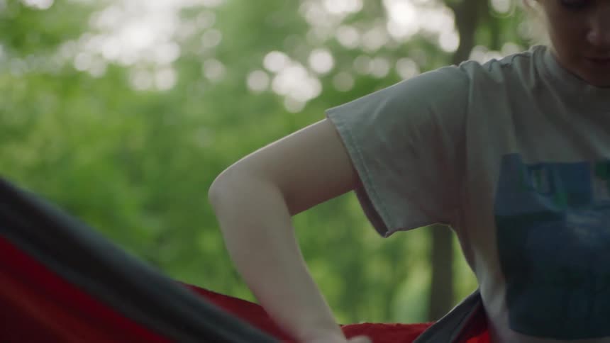A young girl sets a hammock up outside and then sits in it and swings