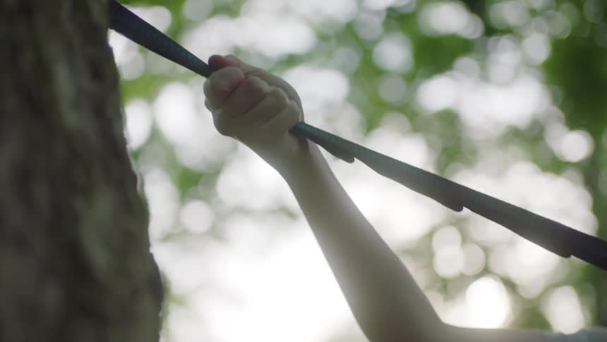 Girl with red hair a grey t shirt sets up a hammock with straps in the forest