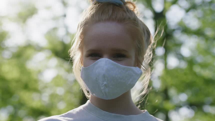Blonde girl wearing face mask stands outdoors in the sunshine