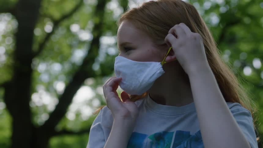 A young girl putting a mask on outside