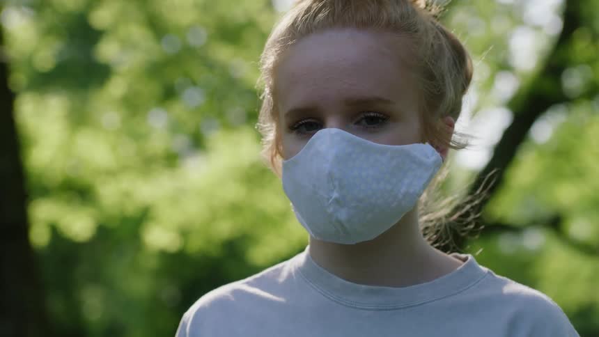 Girl stands outdoor near trees wearing face mask