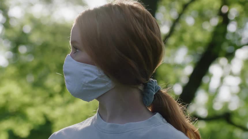 A young woman wearing a face mask turns to look into the camera