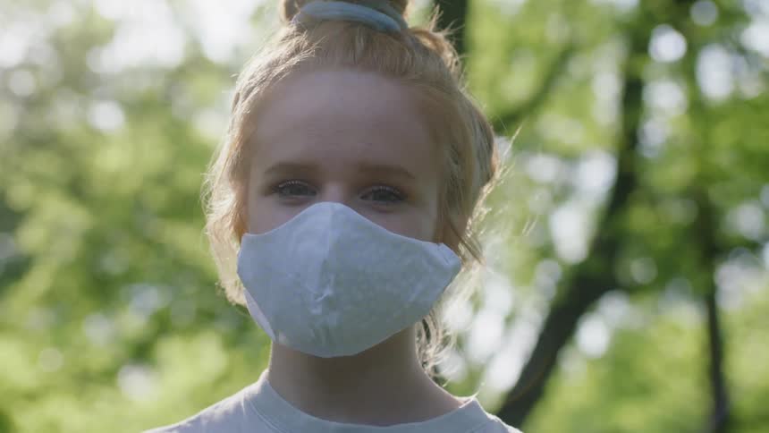 Girl with red hair and a light blue face mask turns her head to camera in the forest