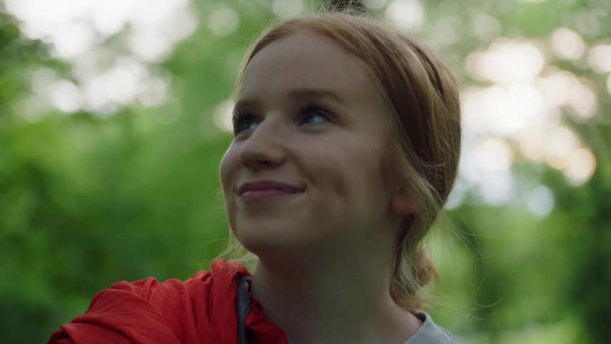 A young woman looks up at the trees smiling