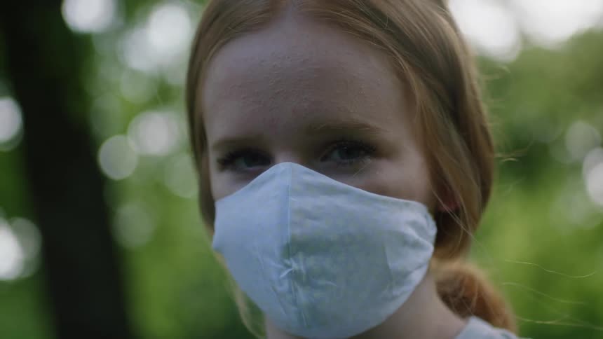 A girl wearing a facemask is standing by the trees