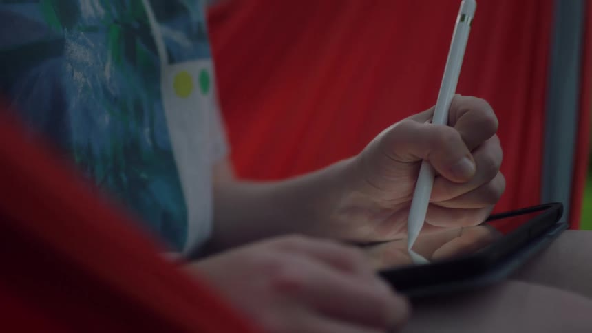 A young girl sits outside and draws on a tablet